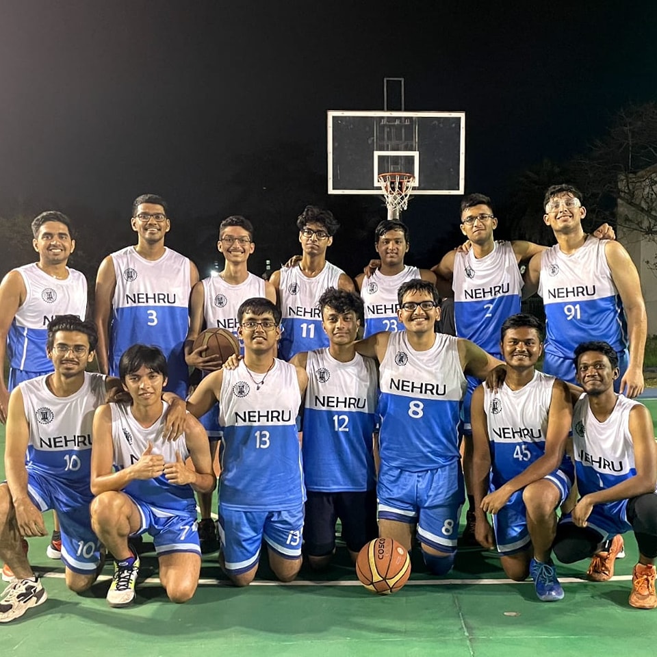 The Nehru Hall basketball team posing together on an outdoor court at night, wearing white-and-blue Nehru jerseys.